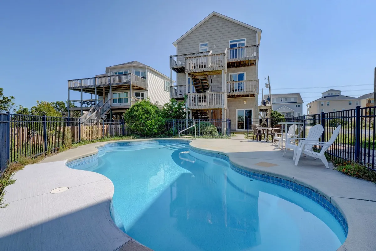 This image features a sparkling swimming pool in the foreground, with children happily splashing in the water. The home's exterior is visible, showcasing balconies with outdoor seating. The setting sun casts a warm glow, and in the background, the scene hints at relaxed, sociable gatherings on the patio.