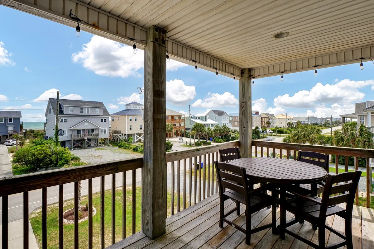 A wooden deck outfitted with an outdoor dining table overlooks the ocean. The wide, unobstructed view offers a serene seascape, ideal for enjoying meals or coffee while listening to the waves. The setting is peaceful and invites relaxation any time of day.