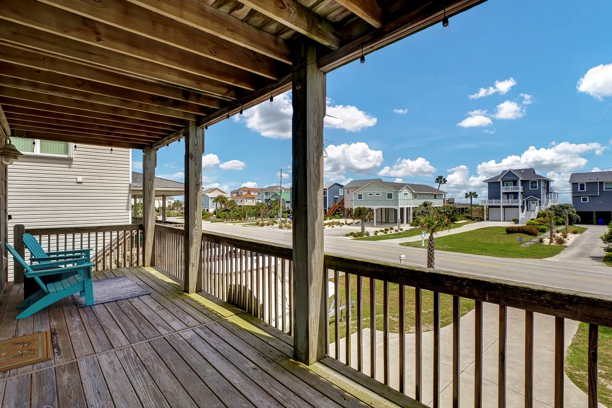 This image features a wooden deck equipped with a blue chair, overlooking surrounding houses and a coastal road. The scene evokes the atmosphere of relaxing on the deck, soaking in the views, and enjoying the gentle ocean breeze. The orientation and furnishings suggest a perfect spot for morning coffee or evening gatherings with friends and family.
