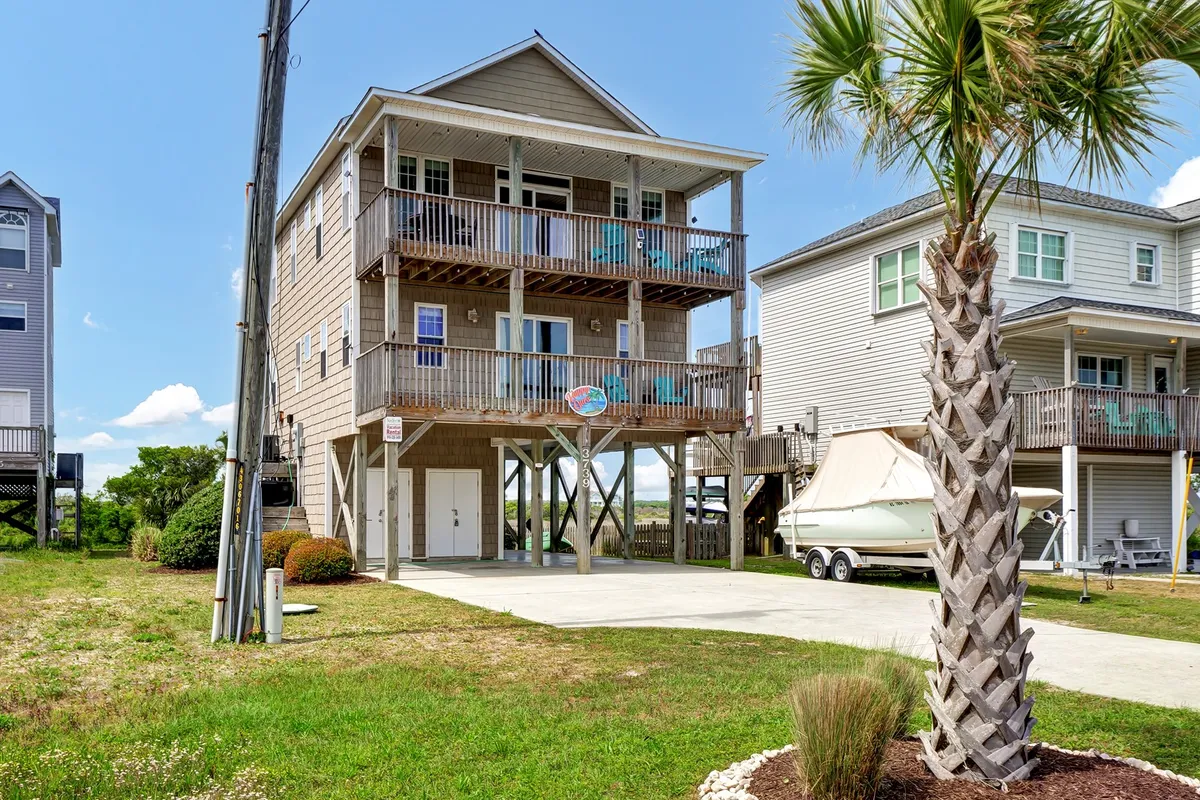 An exterior shot highlighting a three-story house with balconies, a palm tree, and a private driveway. The driveway is spacious and accommodates multiple vehicles or gear, while balconies suggest ample storage and outdoor enjoyment.