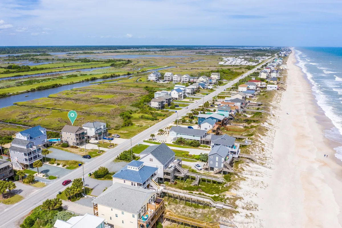 A wide-angle view of beachfront properties lining a scenic coastal road, with ocean waves and marshland in the distance. The landscape blends the tranquility of the sound and the dynamic energy of the ocean, ideal for exploration and quiet getaways.