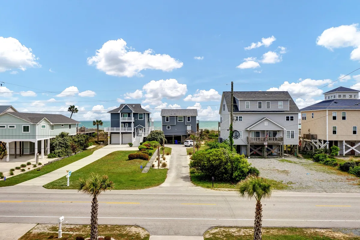 An inviting exterior shot shows beachfront houses framed by palm trees and a road leading directly to the sandy beach. The natural setting exudes relaxation and provides a sense of the wider neighborhood and the proximity to outdoor adventures. This view hints at group beach walks and easy access to the ocean.