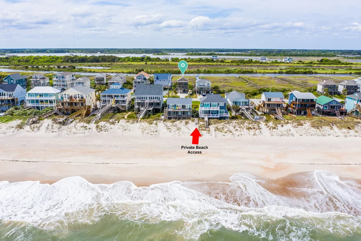A scenic view of beachfront homes with a clear path leading to the sandy shore. The ocean waves are visible, and the lush green landscape frames the private beach access, promising effortless seaside adventures.