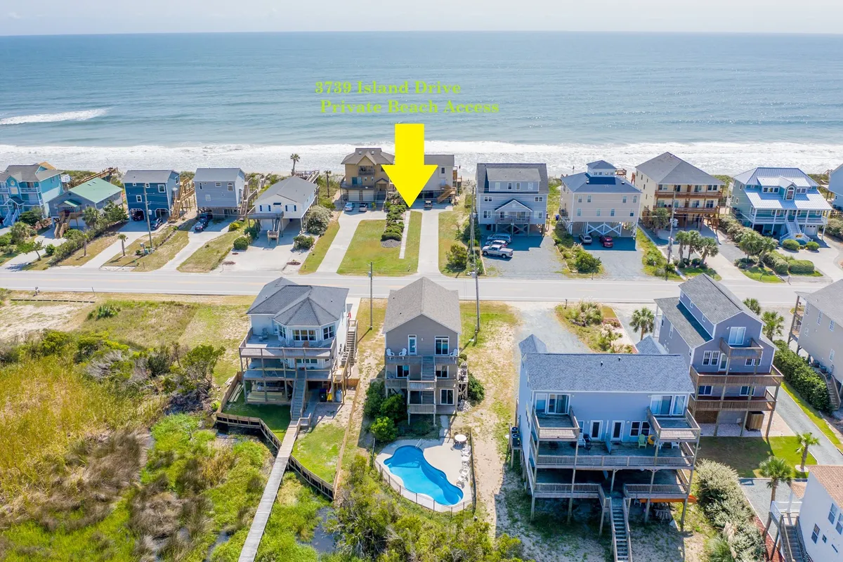 A sunlit exterior scene showing houses directly across from the wide sandy beachfront, with a sparkling swimming pool in the foreground and families enjoying both the pool and the beach. The image captures the proximity of the property to the beach and features families engaged in swimming and beachcombing, with inviting sunset lighting.