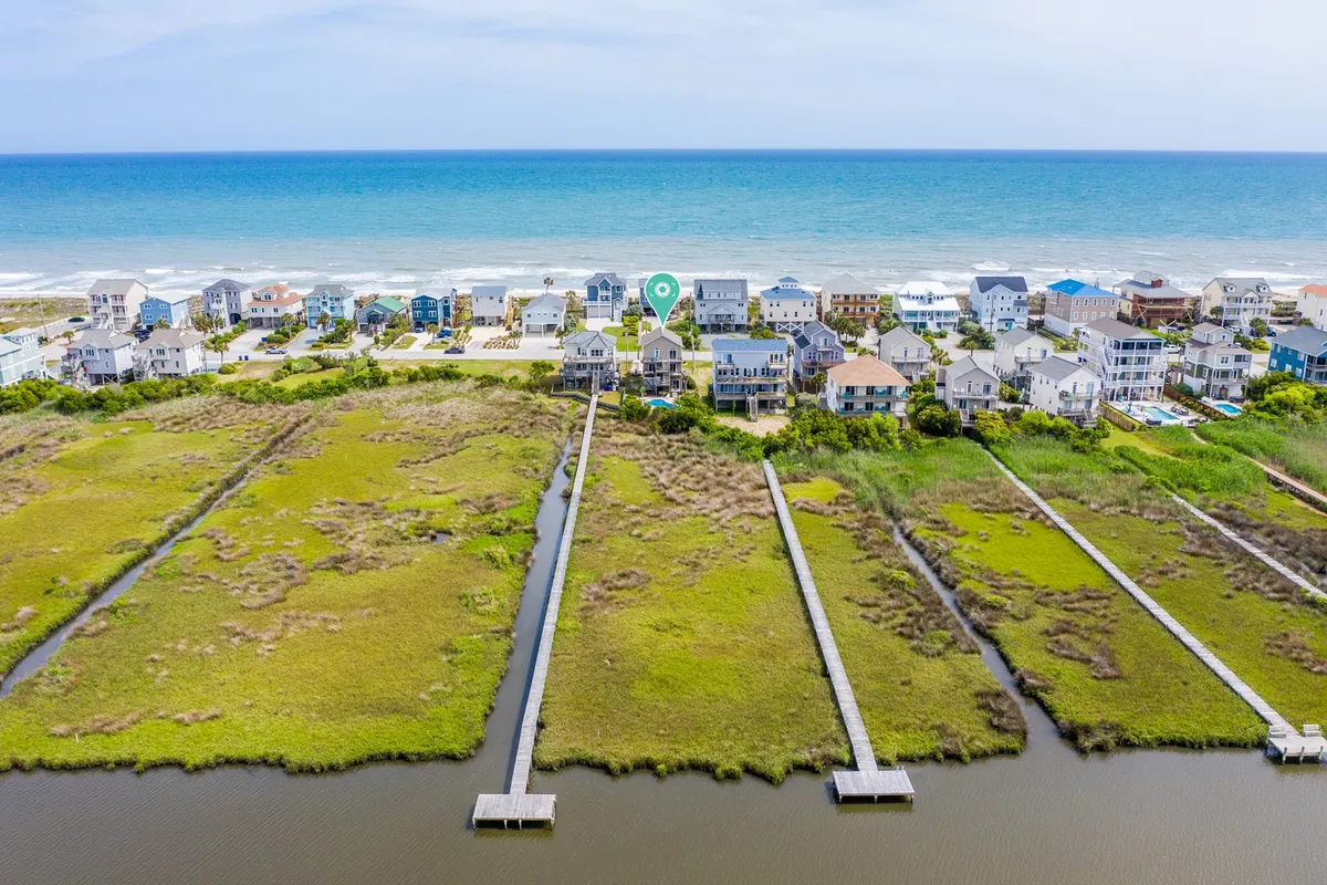 This image presents a panoramic exterior view of oceanfront boardwalks, inviting sandy beach, and marshland with beach houses in the background. The scene is bathed in soft natural light, evoking a tranquil, romantic atmosphere ideal for morning or sunset strolls.