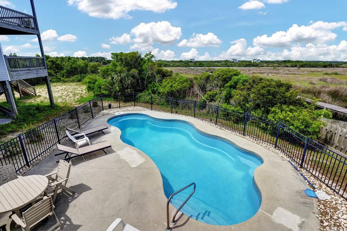 An exterior shot of a sparkling swimming pool surrounded by lush greenery and comfortable patio furniture. The setting is private and inviting, suggesting leisurely afternoons spent poolside in a relaxing, resort-like atmosphere.