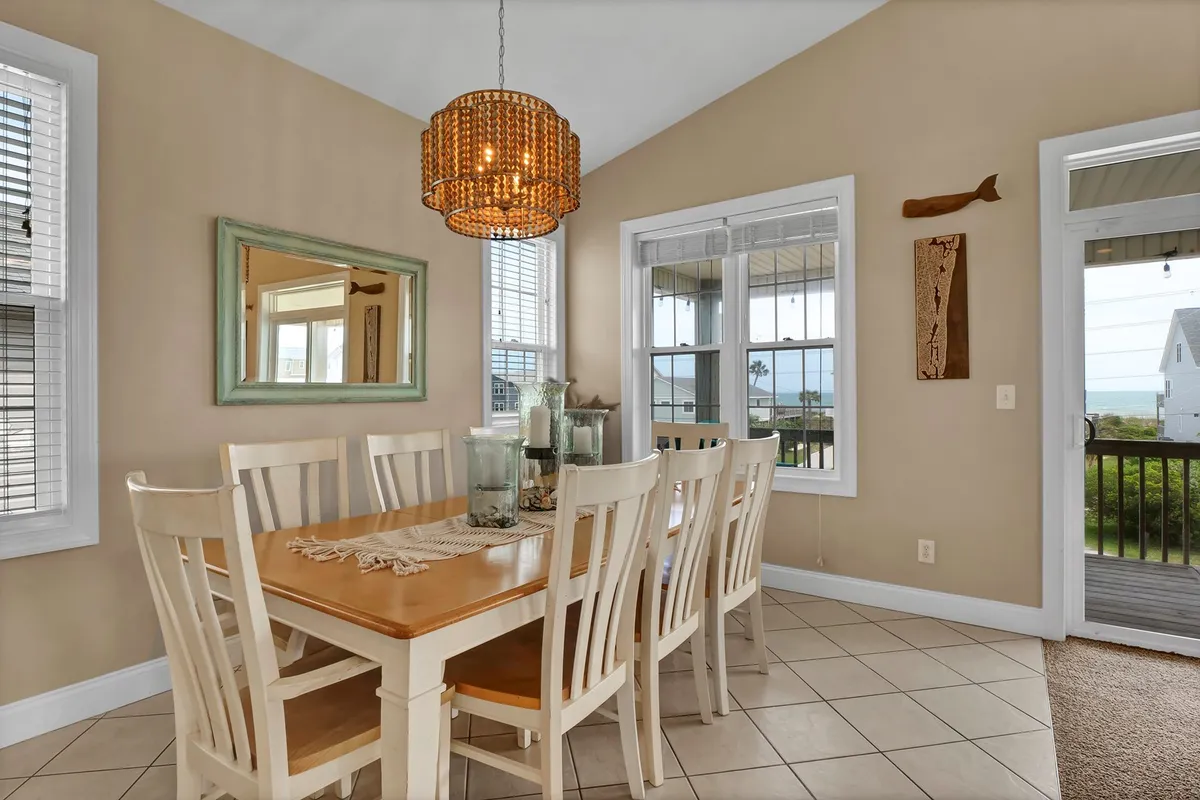 This photo focuses on the inviting dining area, featuring a large table set for eight beneath an elegant chandelier, with windows showcasing a scenic backdrop. The arrangement highlights space for shared meals and special occasions, with natural light enhancing the warmth and comfort of the setting.