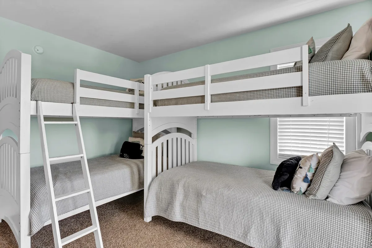 A playful and inviting twin bunk room with plaid bedding and decorative pillows, designed for kids or teens. The room is colorful and fun, perfect for imaginative adventures and cozy night-time chats.
